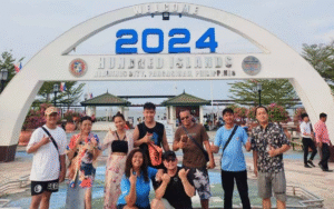 Tour group posing under a 2024 welcome arch at an event in the Philippines